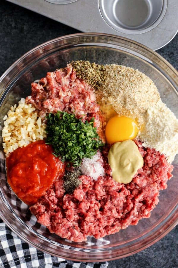 Italian Meatloaf Muffins turns your favorite meatloaf into muffins with gooey mozzarella cheese centers and savory herbs. Meatloaf ingredients in a clear bowl.