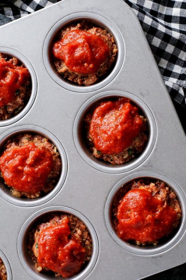 Italian Meatloaf Muffins turns your favorite meatloaf into muffins with gooey mozzarella cheese centers and savory herbs. Close up shot of meatloaf muffins with marinara sauce on top.