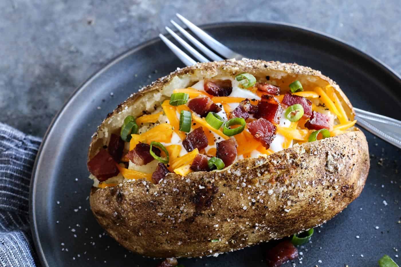 This baked potato recipe makes fluffy, tender potatoes with salty, crispy skin! Learn how to bake potatoes in the oven, plus 3 more ways! baked potato on a plate, topped with cheese and bacon