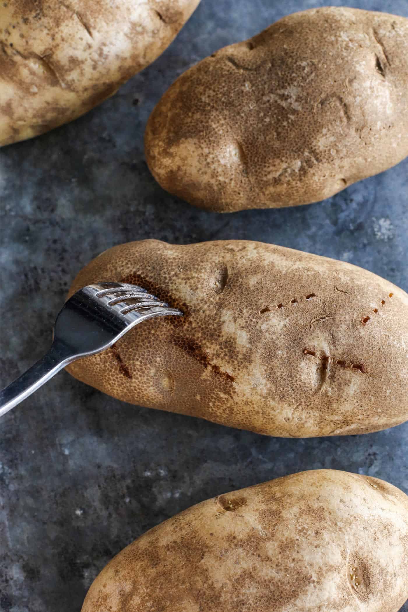This baked potato recipe makes fluffy, tender potatoes with salty, crispy skin! Learn how to bake potatoes in the oven, plus 3 more ways! a fork poking Russet potatoes