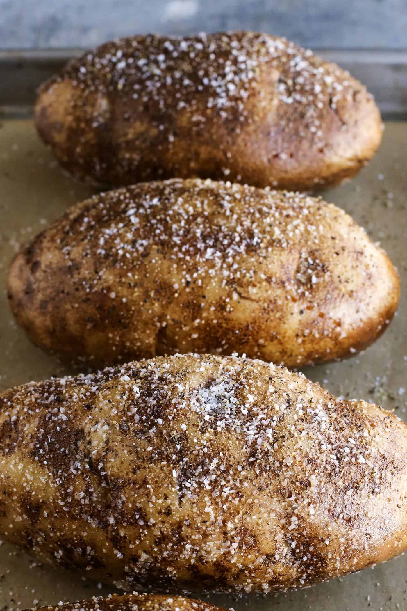 This baked potato recipe makes fluffy, tender potatoes with salty, crispy skin! Learn how to bake potatoes in the oven, plus 3 more ways! large potatoes on a baking pan, with olive oil, salt, pepper, and garlic powder