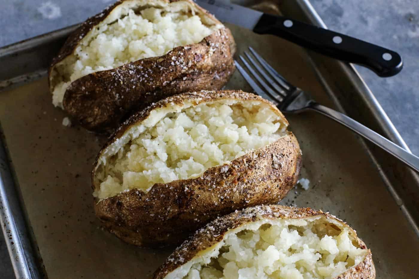 This baked potato recipe makes fluffy, tender potatoes with salty, crispy skin! Learn how to bake potatoes in the oven, plus 3 more ways! oven baked potatoes cut open on a pan