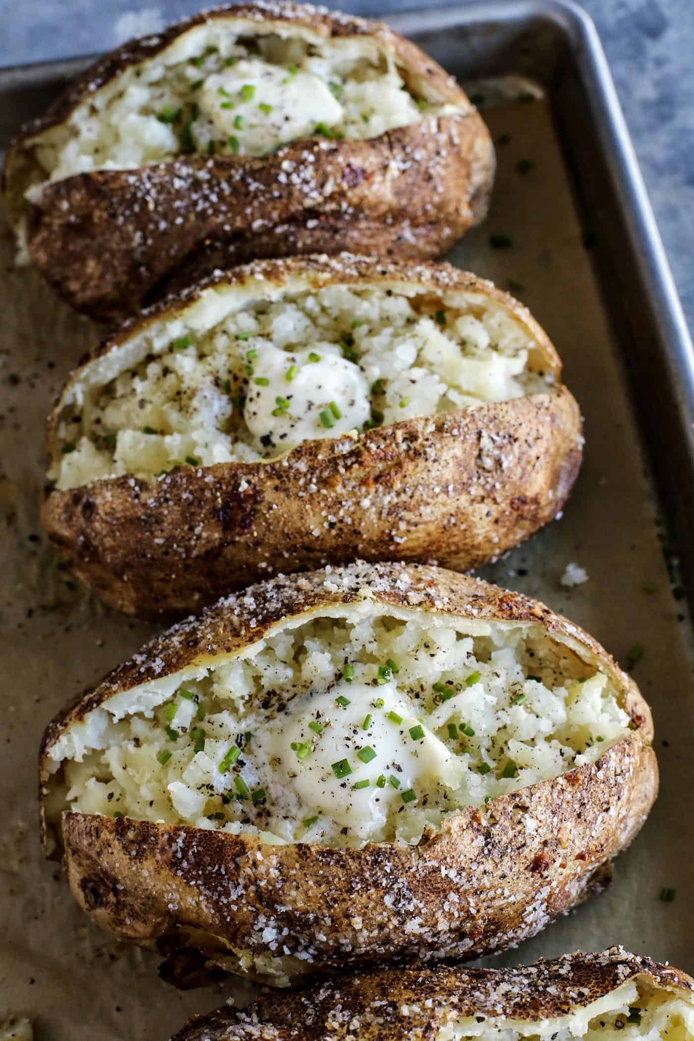 This baked potato recipe makes fluffy, tender potatoes with salty, crispy skin! Learn how to bake potatoes in the oven, plus 3 more ways! potatoes baked in the oven, split open, with butter and chives