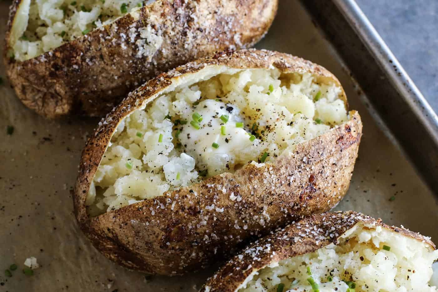 This baked potato recipe makes fluffy, tender potatoes with salty, crispy skin! Learn how to bake potatoes in the oven, plus 3 more ways! butter and chives on baked potatoes