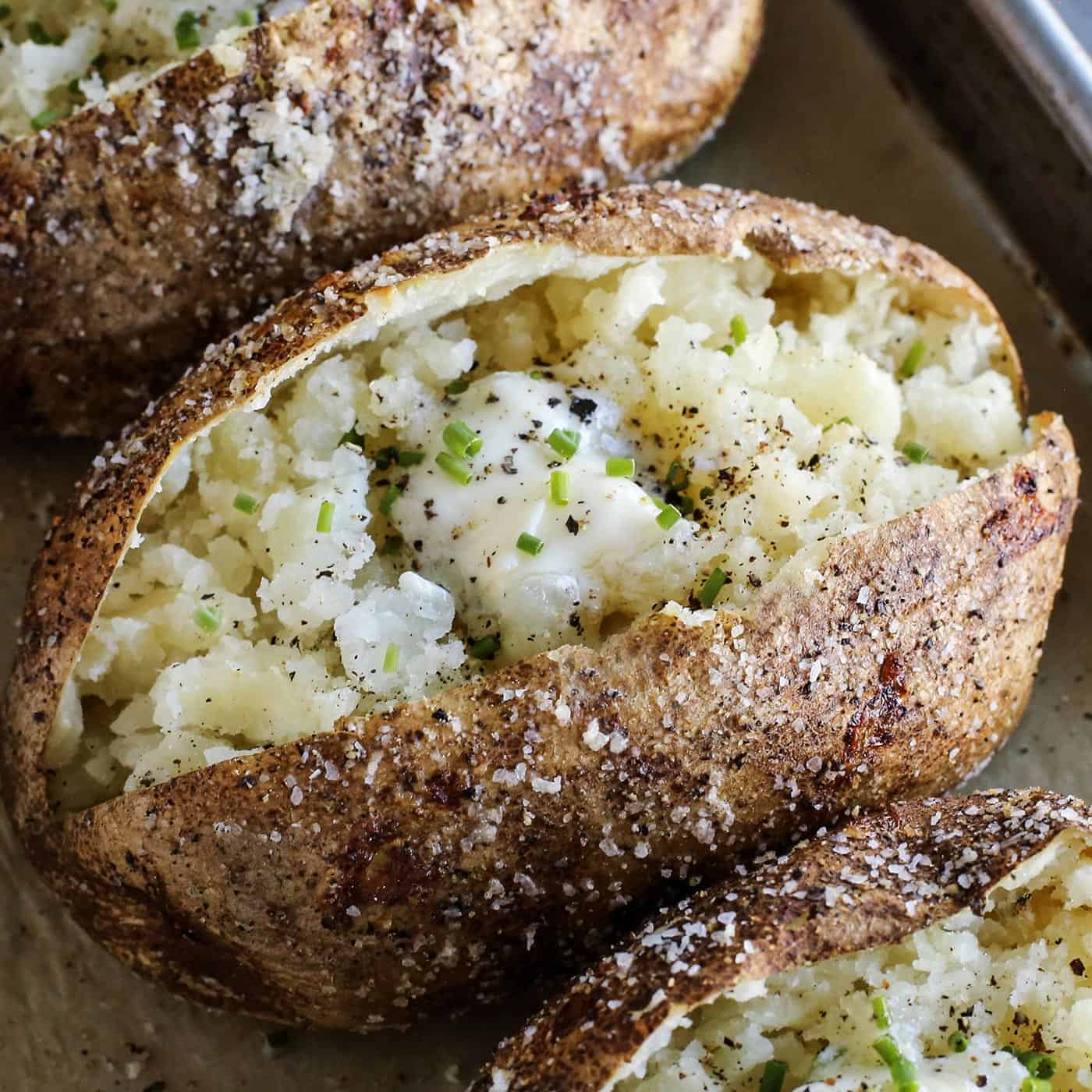 This baked potato recipe makes fluffy, tender potatoes with salty, crispy skin! Learn how to bake potatoes in the oven, plus 3 more ways! baked potato cut open, with crispy skin and tender insides