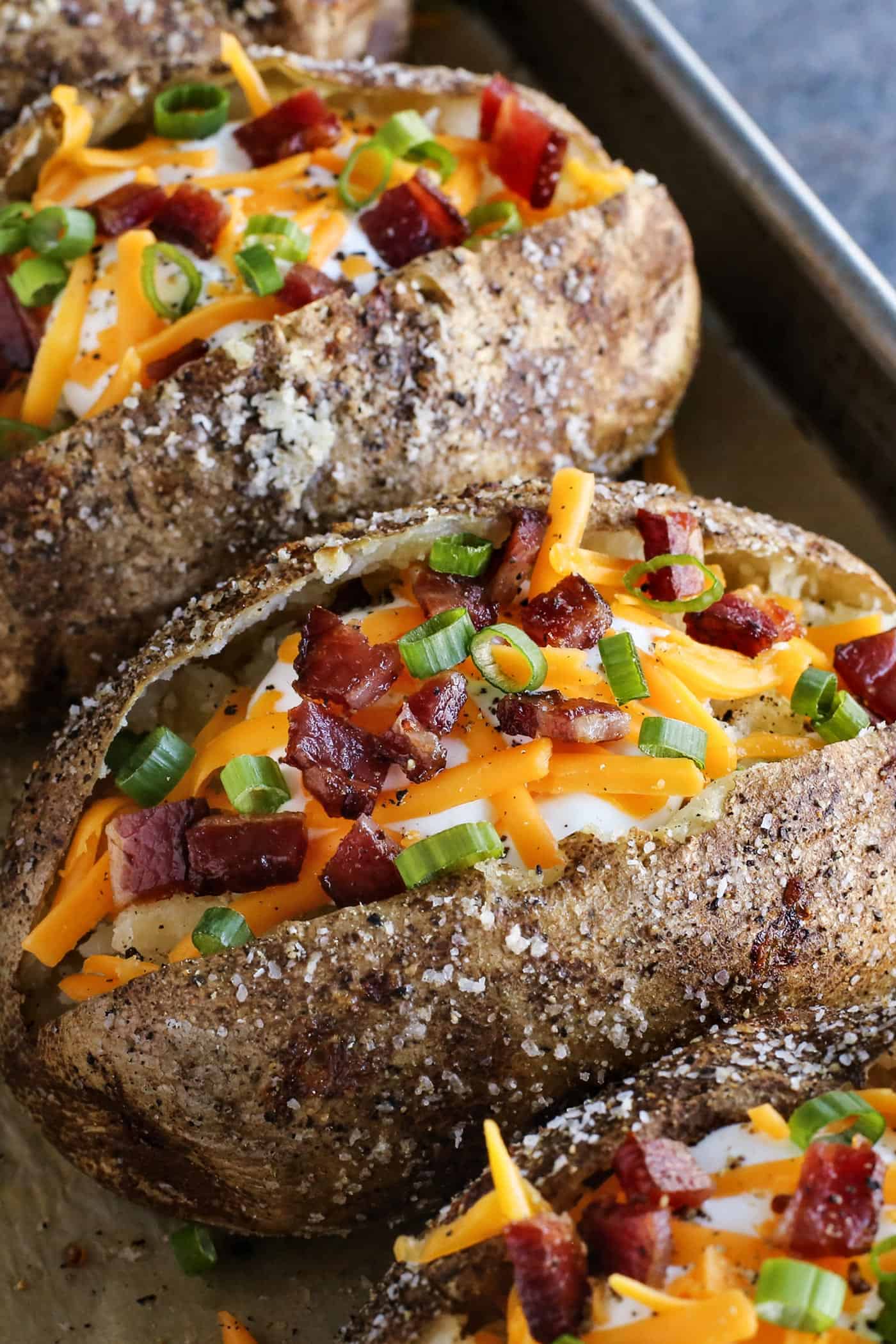 This baked potato recipe makes fluffy, tender potatoes with salty, crispy skin! Learn how to bake potatoes in the oven, plus 3 more ways! baked potatoes split open and topped with cheese and bacon
