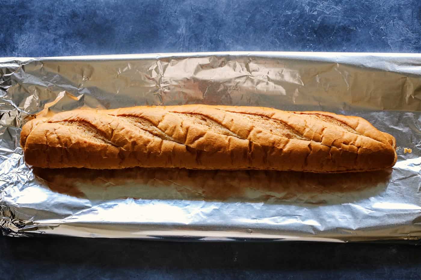 Cheesy garlic bread is the best, with buttery, toasted bread that's soft inside, crispy outside, and loaded with fresh herbs and melty cheese. A loaf of French bread on a foil-lined baking sheet.
