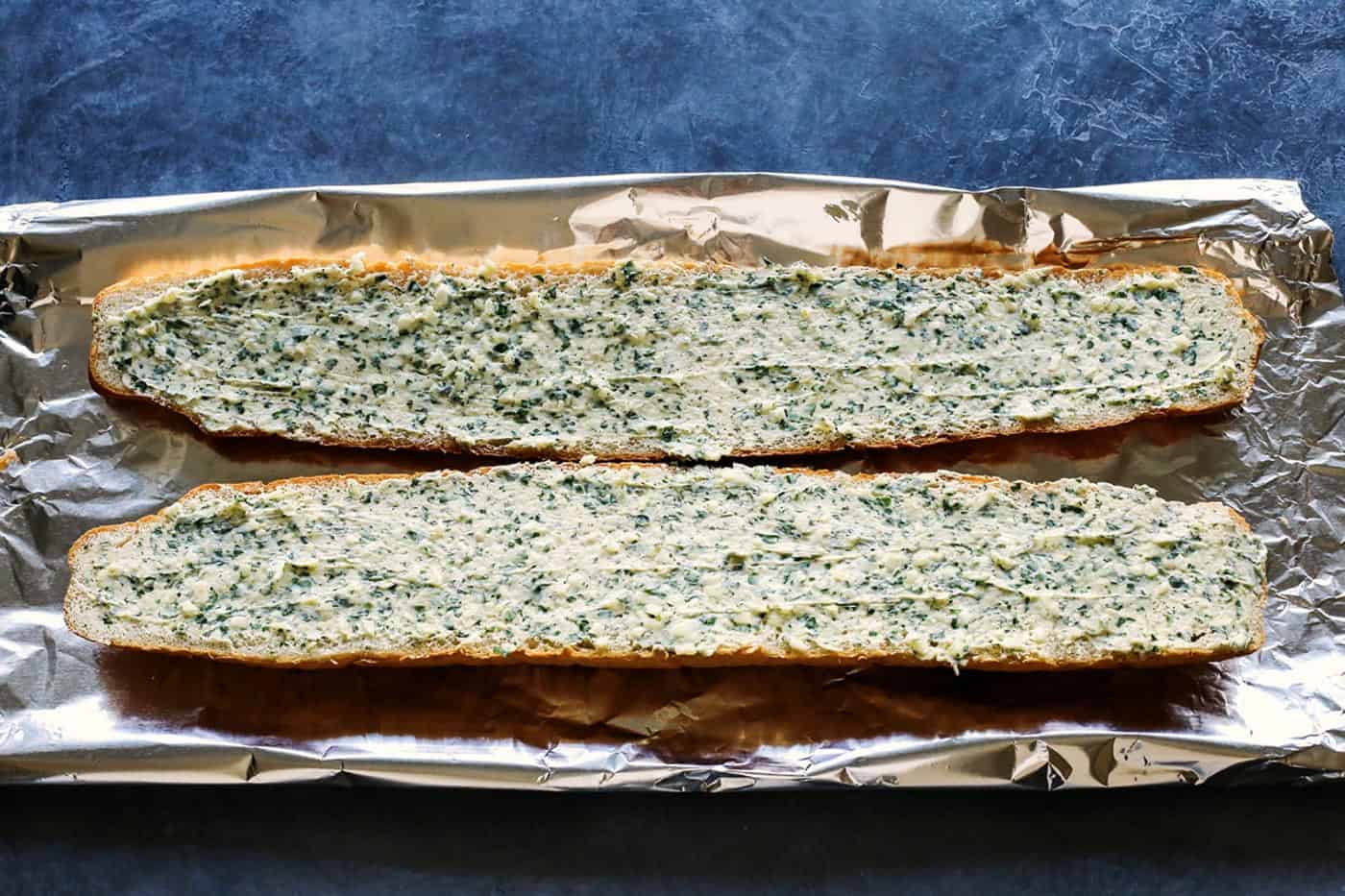 Cheesy garlic bread is the best, with buttery, toasted bread that's soft inside, crispy outside, and loaded with fresh herbs and melty cheese. Two halves of a bread loaf spread with garlic butter on a baking sheet.