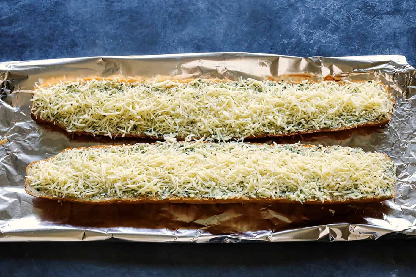Cheesy garlic bread is the best, with buttery, toasted bread that's soft inside, crispy outside, and loaded with fresh herbs and melty cheese. Two halves of a bread loaf spread with garlic butter and topped with shredded cheese on a baking sheet.