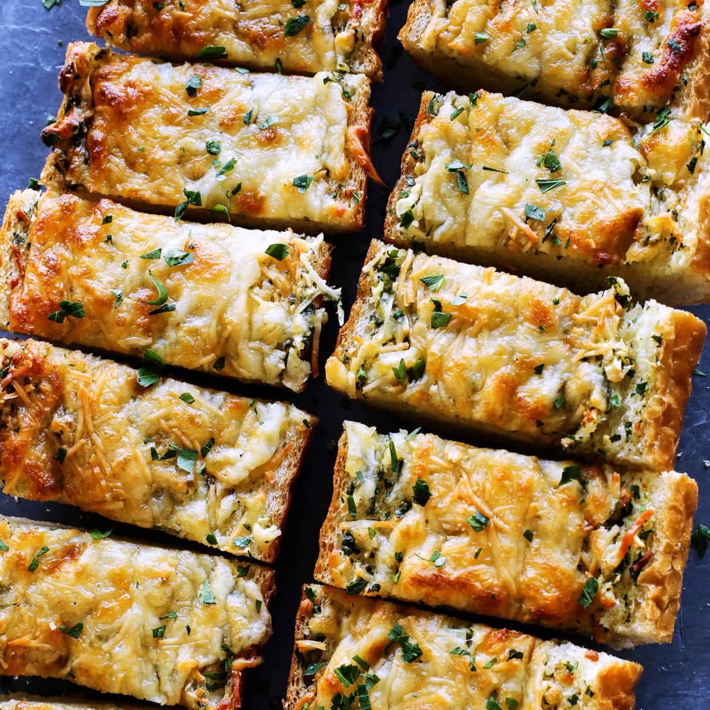 Cheesy garlic bread is the best, with buttery, toasted bread that's soft inside, crispy outside, and loaded with fresh herbs and melty cheese. Overhead view of cheesy garlic bread cut into slices.