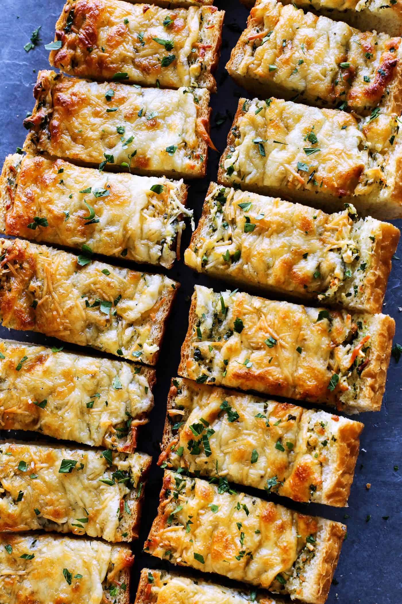 Cheesy garlic bread is the best, with buttery, toasted bread that's soft inside, crispy outside, and loaded with fresh herbs and melty cheese. Overhead view of cheesy garlic bread cut into slices.