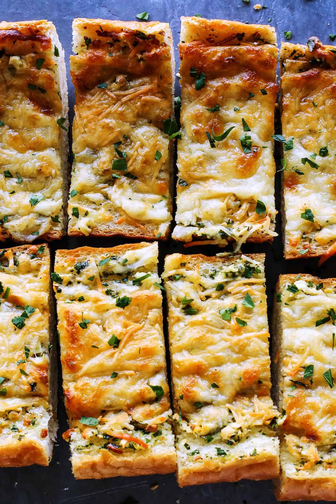 Cheesy garlic bread is the best, with buttery, toasted bread that's soft inside, crispy outside, and loaded with fresh herbs and melty cheese. Overhead view of cheesy garlic bread cut into slices.