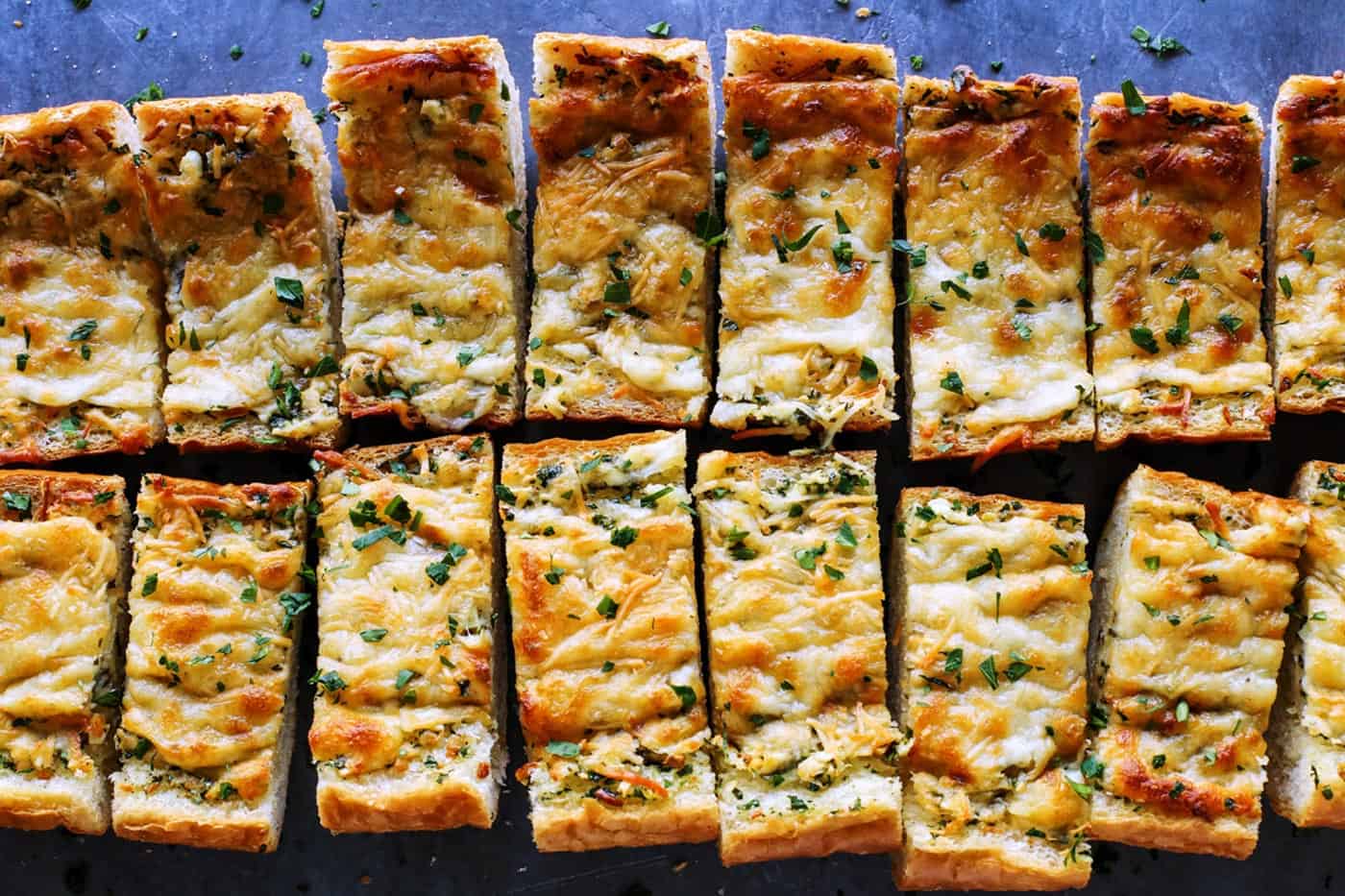 Cheesy garlic bread is the best, with buttery, toasted bread that's soft inside, crispy outside, and loaded with fresh herbs and melty cheese. Overhead view of cheesy garlic bread cut into slices.