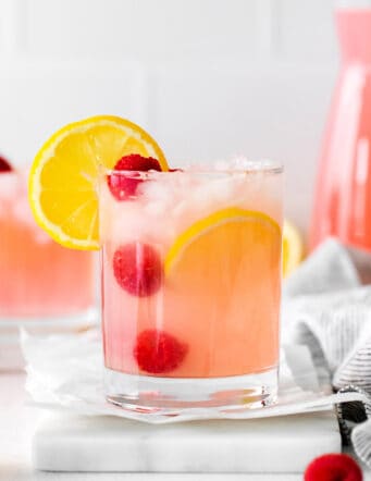 A pink lemonade margarita garnished with raspberries and lemon