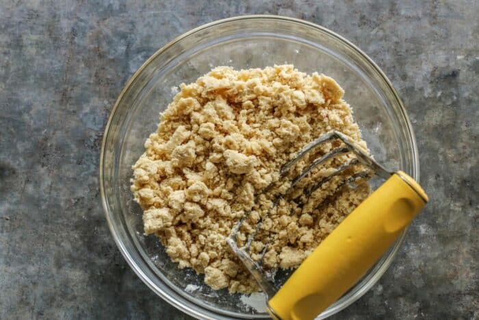 Strawberry Rhubarb Crumble is an easy dessert recipe with a sweet-tart, jammy fruit filling plus a buttery, crispy topping. making crumble topping in a clear bowl, with a rigid pastry cutter
