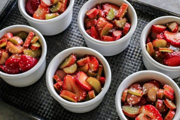 Strawberry Rhubarb Crumble is an easy dessert recipe with a sweet-tart, jammy fruit filling plus a buttery, crispy topping. sliced strawberries and rhubarb in ramekins on a metal pan