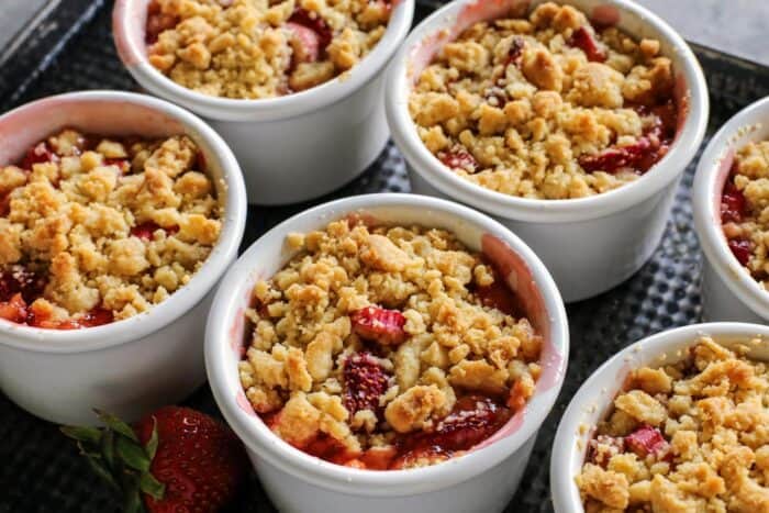Strawberry Rhubarb Crumble is an easy dessert recipe with a sweet-tart, jammy fruit filling plus a buttery, crispy topping. ramekins on a pan, filled with a baked crumble that includes rhubarb and strawberries