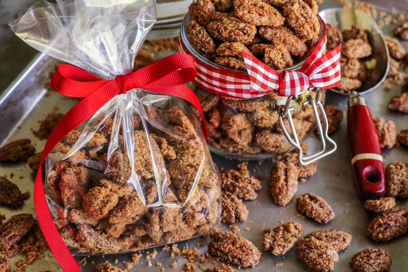Crunchy candied pecans recipe for a sweet and salty treat with just a hint of heat. The perfect snack, salad topper, or edible gift! candied pecans in a small clear bar with a red ribbon and in a jar with red gingham ribbon