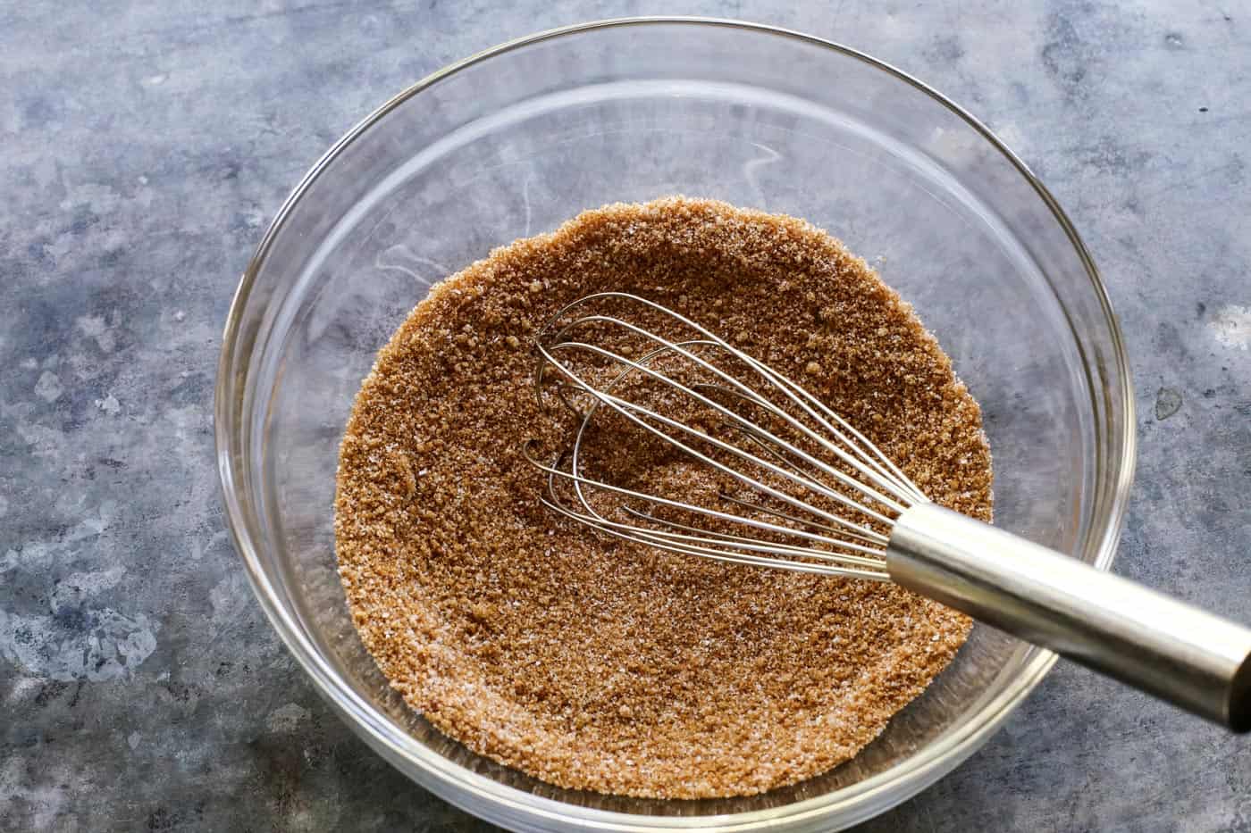 Crunchy candied pecans recipe for a sweet and salty treat with just a hint of heat. The perfect snack, salad topper, or edible gift! whisk and clear bowl with a mixture of sugars, salt, cayenne, and cinnamon
