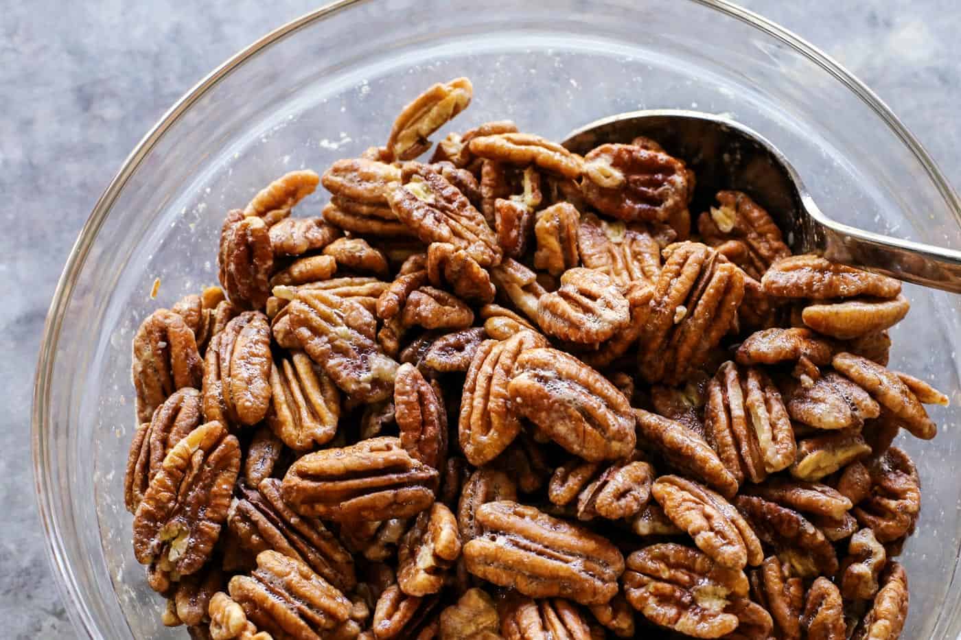Crunchy candied pecans recipe for a sweet and salty treat with just a hint of heat. The perfect snack, salad topper, or edible gift! a bowl of pecans coated in whipped egg white