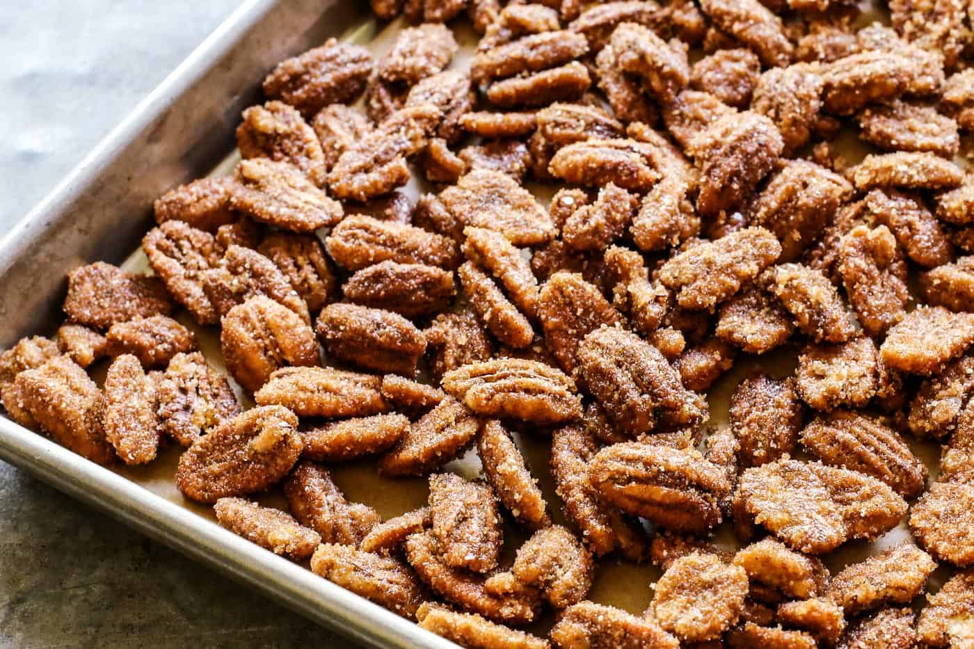 Crunchy candied pecans recipe for a sweet and salty treat with just a hint of heat. The perfect snack, salad topper, or edible gift! sugar-coated pecans spread out on a rimmed baking pan