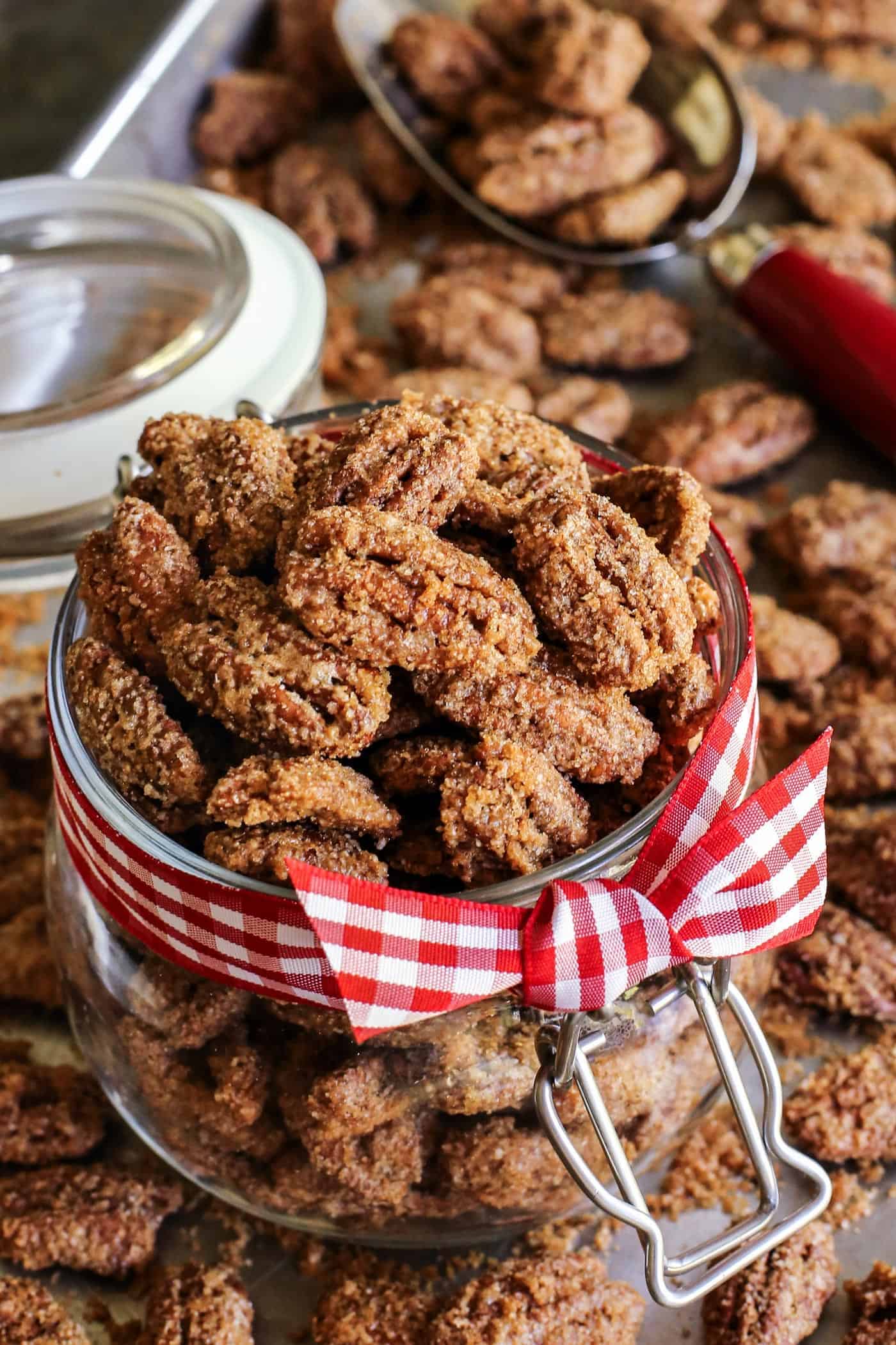 Crunchy candied pecans recipe for a sweet and salty treat with just a hint of heat. The perfect snack, salad topper, or edible gift! candied whole pecans in a jar with a red gingham ribbon tied around it