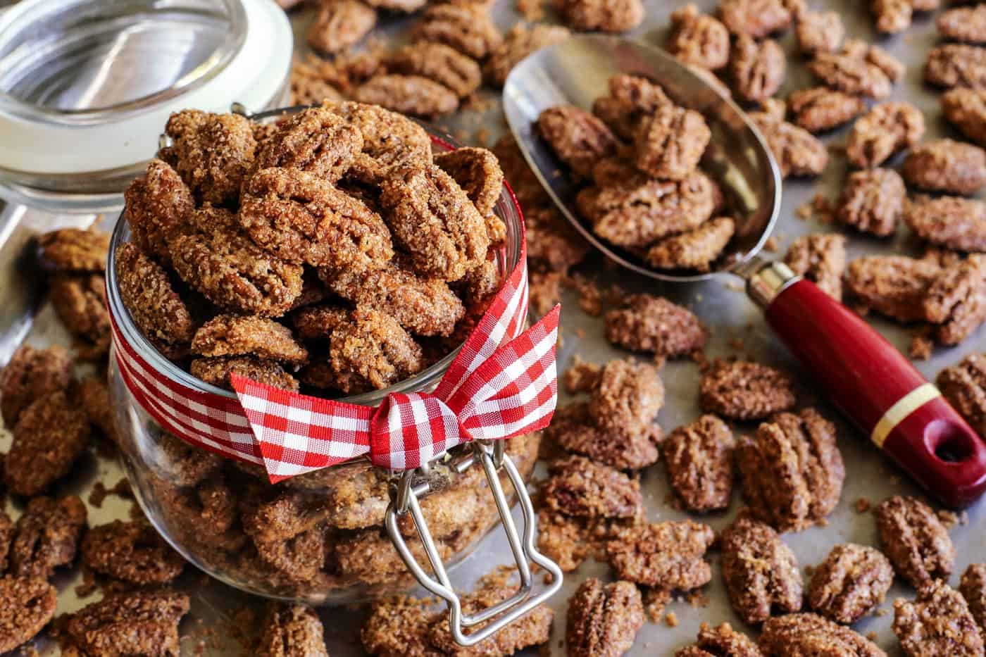 Crunchy candied pecans recipe for a sweet and salty treat with just a hint of heat. The perfect snack, salad topper, or edible gift! a pan of baked candied pecans, some of the pecans are in a jar