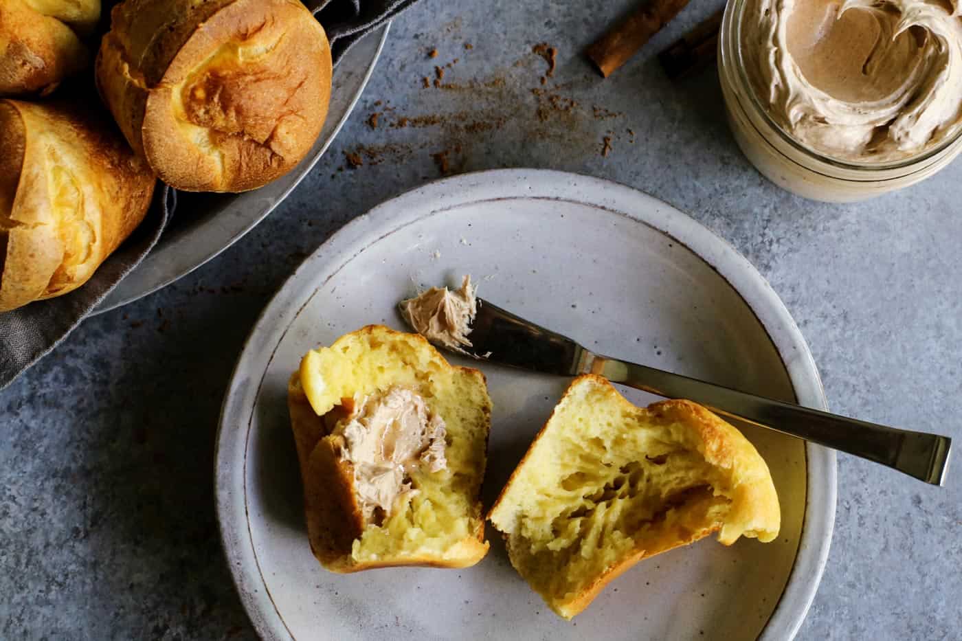 This easy cinnamon honey butter is whipped, fluffy, and even better than Texas Roadhouse butter! Make it with 5 ingredients in 10 minutes! Overhead view of a popover on a plate with one half spread with cinnamon honey butter.
