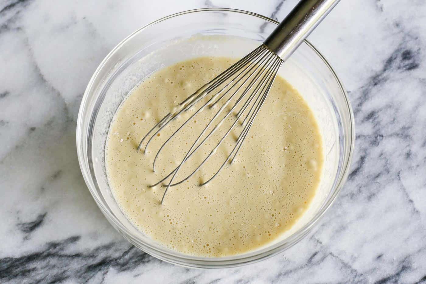 Popovers bake up tall, golden, and airy with crisp edges and soft centers, using only 4 simple ingredients and an easy, foolproof method! Bowl of popover batter with a whisk in it.