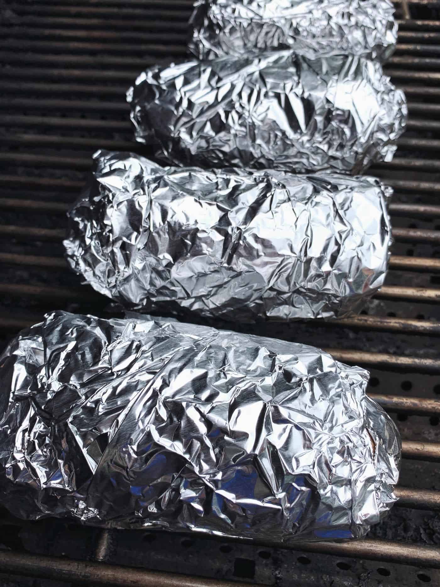 This baked potato recipe makes fluffy, tender potatoes with salty, crispy skin! Learn how to bake potatoes in the oven, plus 3 more ways! potatoes wrapped in foil on a grill