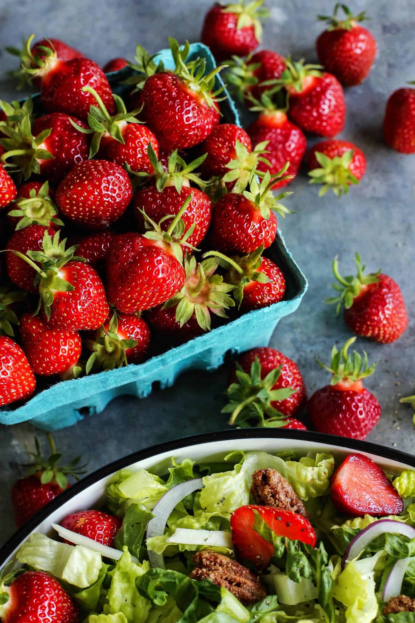 This strawberry salad with red wine vinaigrette has Monterey Jack cheese and ridiculously crunchy candied pecans. It's a crowd-pleaser! an aqua market container full of fresh strawberries set next to salad