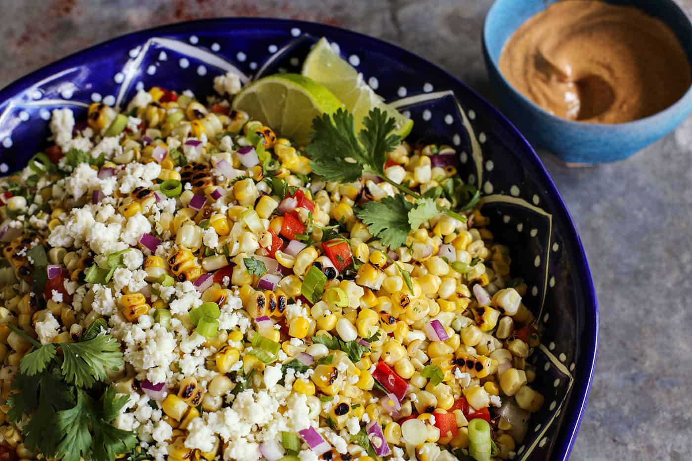 This Mexican Corn Salad, known as esquites, features grilled corn, a tangy, creamy dressing, and plenty of spice. salad made with fresh sweet corn, in a blue pottery bowl