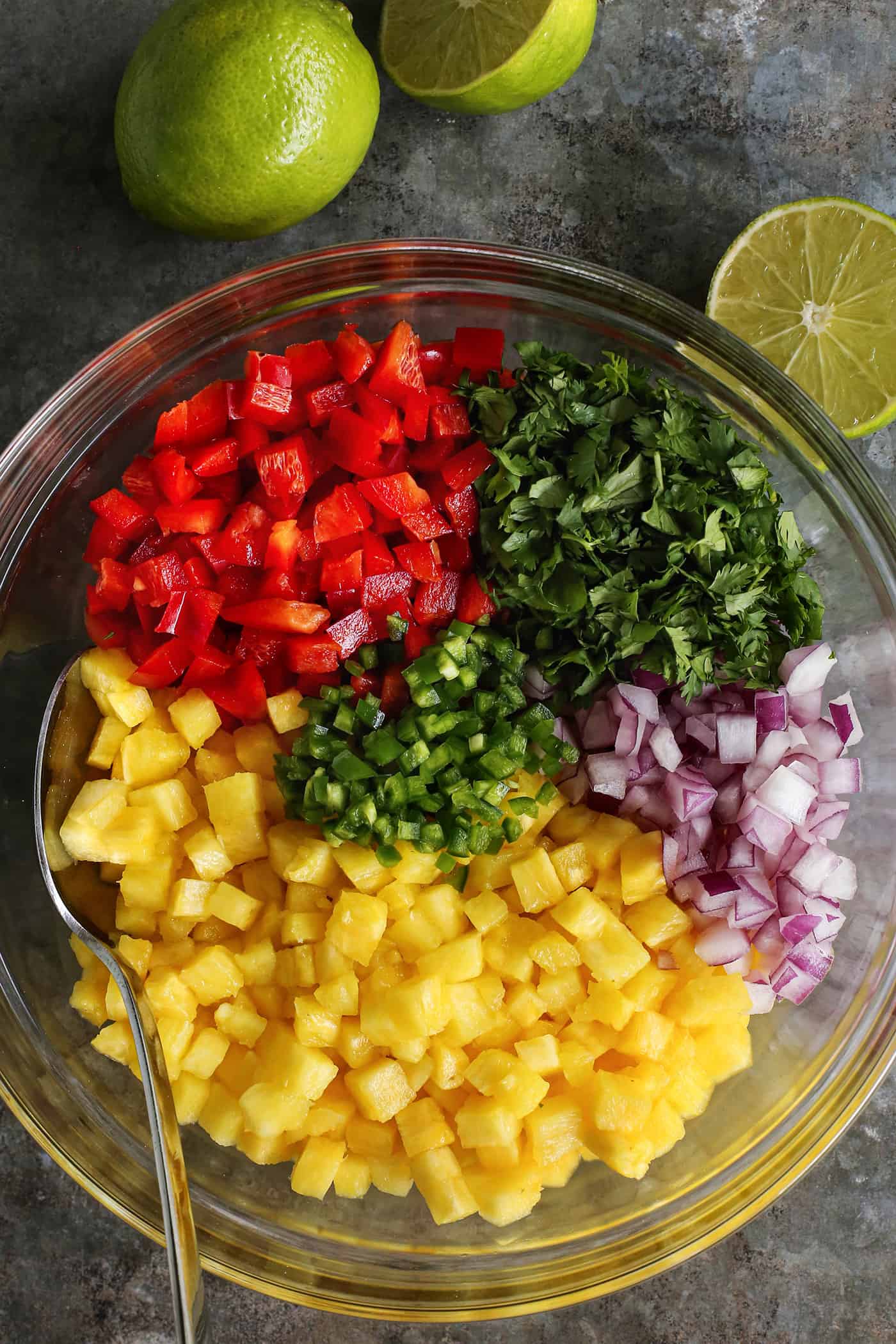 This easy, fresh Pineapple Salsa recipe makes for a fun party appetizer or a juicy condiment for tacos, salads, and grilled meats and fish. a large clear bowl with diced pineapple, red pepper, red onion, jalapeno, and cilantro, plus fresh limes