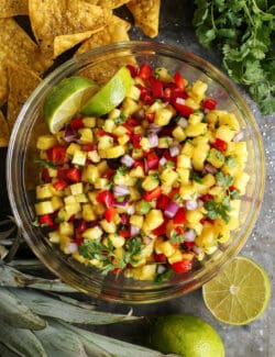 large clear bowl of pineapple salsa, plus tortilla chips and limes