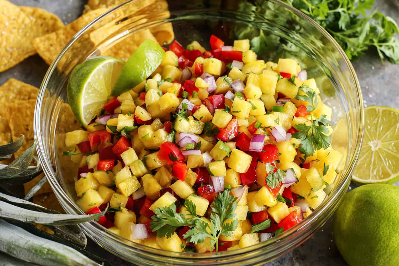 This easy, fresh Pineapple Salsa recipe makes for a fun party appetizer or a juicy condiment for tacos, salads, and grilled meats and fish. a large clear bowl of homemade pineapple salsa, plus chips and limes