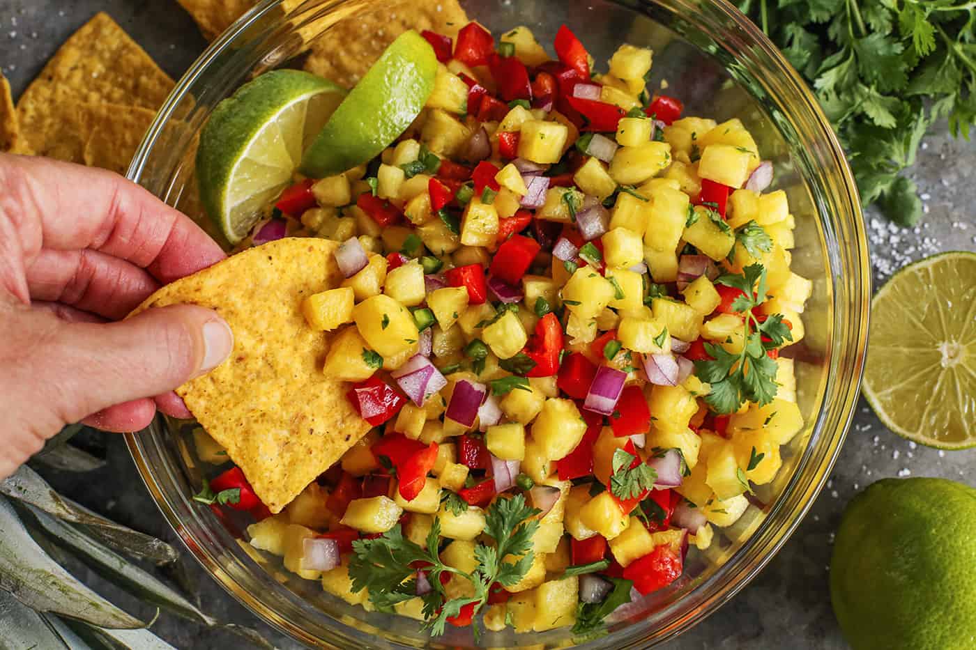 This easy, fresh Pineapple Salsa recipe makes for a fun party appetizer or a juicy condiment for tacos, salads, and grilled meats and fish. hand dipping a tortilla chip into fresh salsa