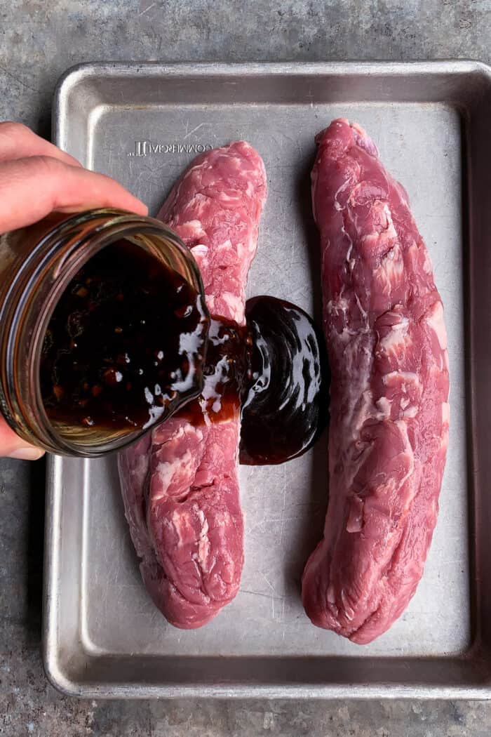 Teriyaki Pork Tenderloin bathes tender pork in a homemade marinade, grills it to perfection, and tops it with juicy fresh pineapple salsa. pouring teriyaki sauce over pork tenderloin on a rimmed pan