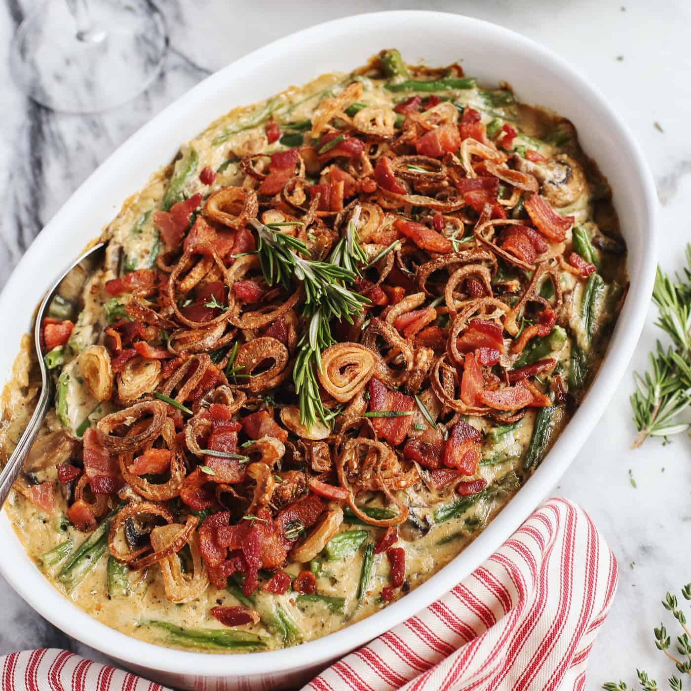 This from-scratch Green Bean Casserole features fresh green beans, crispy bacon, fried shallots, and a creamy homemade gravy. A large dish of bacon and shallot-topped green bean casserole.
