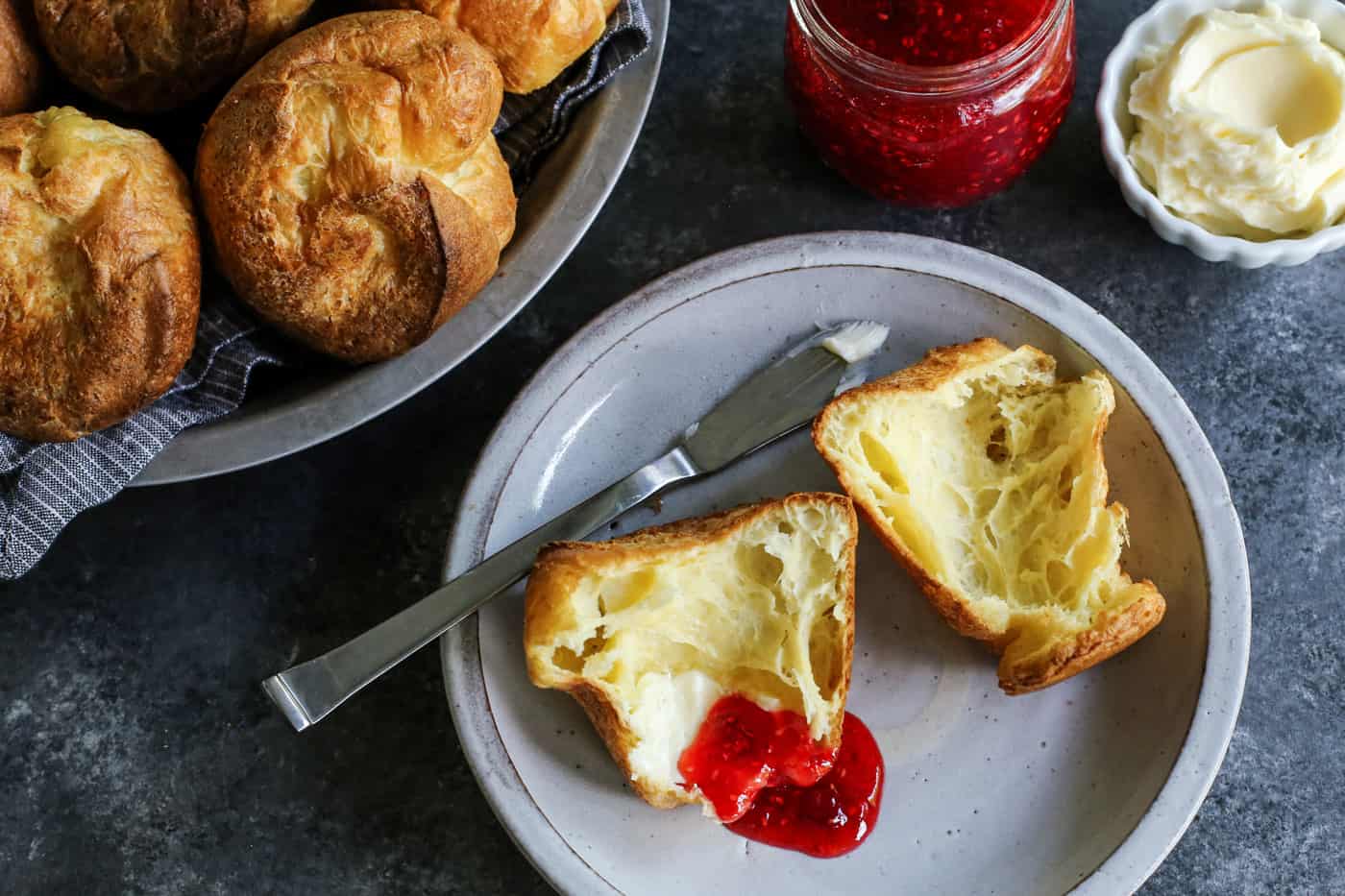 Popovers bake up tall, golden, and airy with crisp edges and soft centers, using only 4 simple ingredients and an easy, foolproof method! A popover split open on a plate, with butter and jam.