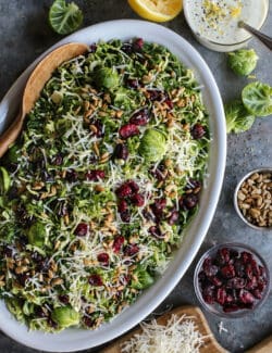 Shaved Brusssels sprouts salad on an oval white platter with a jar of lemon yogurt dressing.