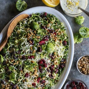 Shaved Brusssels sprouts salad on an oval white platter with a jar of lemon yogurt dressing.