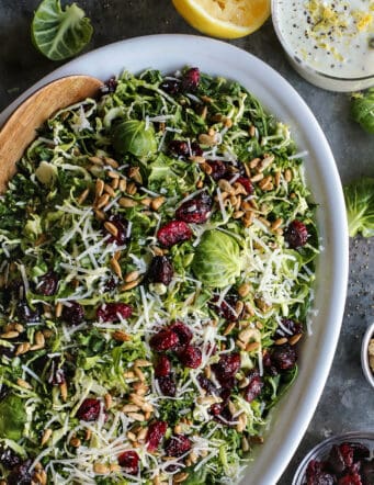 Shaved Brusssels sprouts salad on an oval white platter with a jar of lemon yogurt dressing.