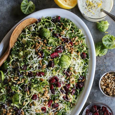 Shaved Brusssels sprouts salad on an oval white platter with a jar of lemon yogurt dressing.