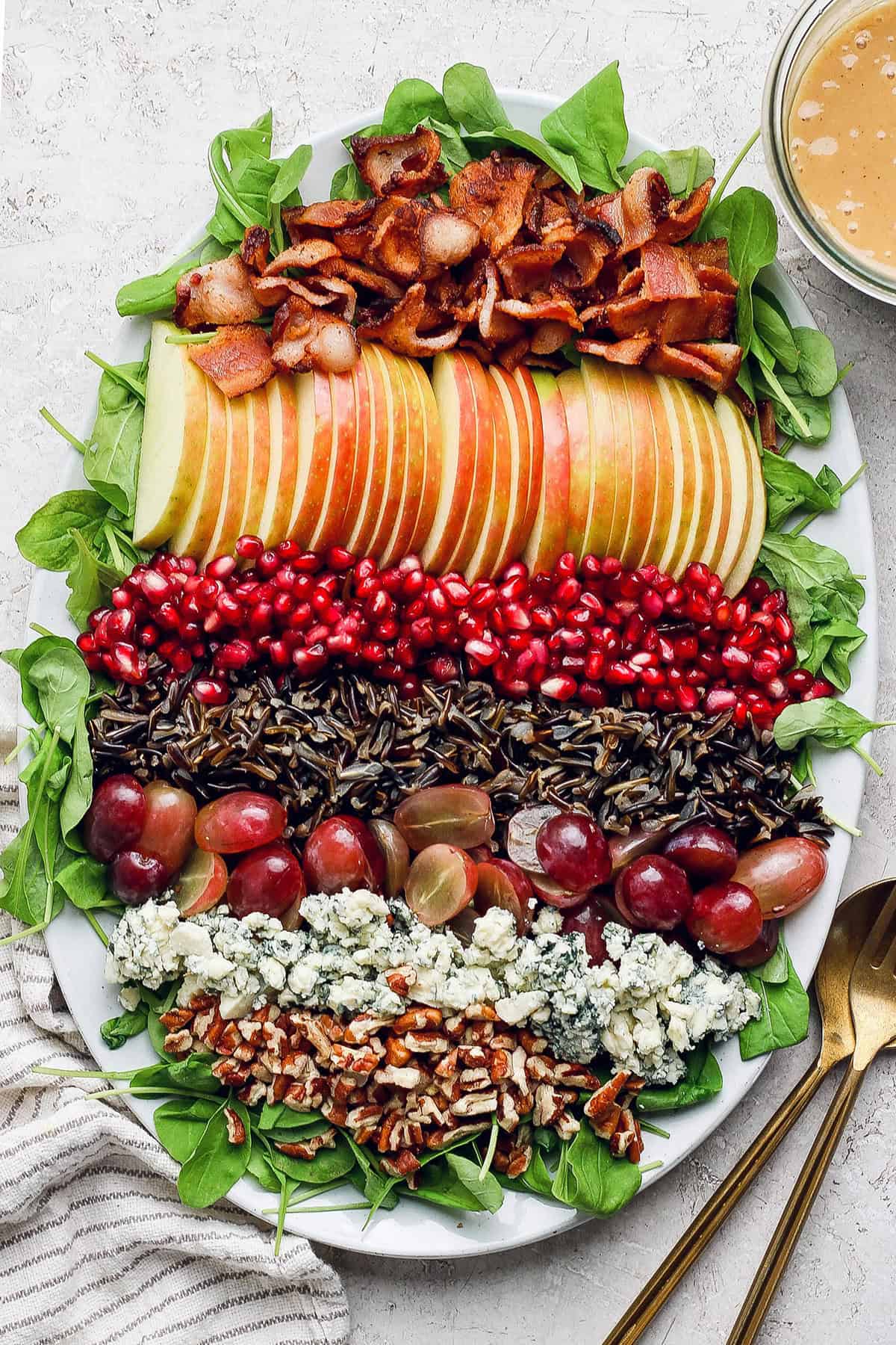 This hearty wild rice salad with pomegranate seeds, blue cheese, pecans, and maple-Dijon dressing is perfect for the holiday season. Assembled wild rice salad on the serving platter with maple-Dijon dressing on the side.