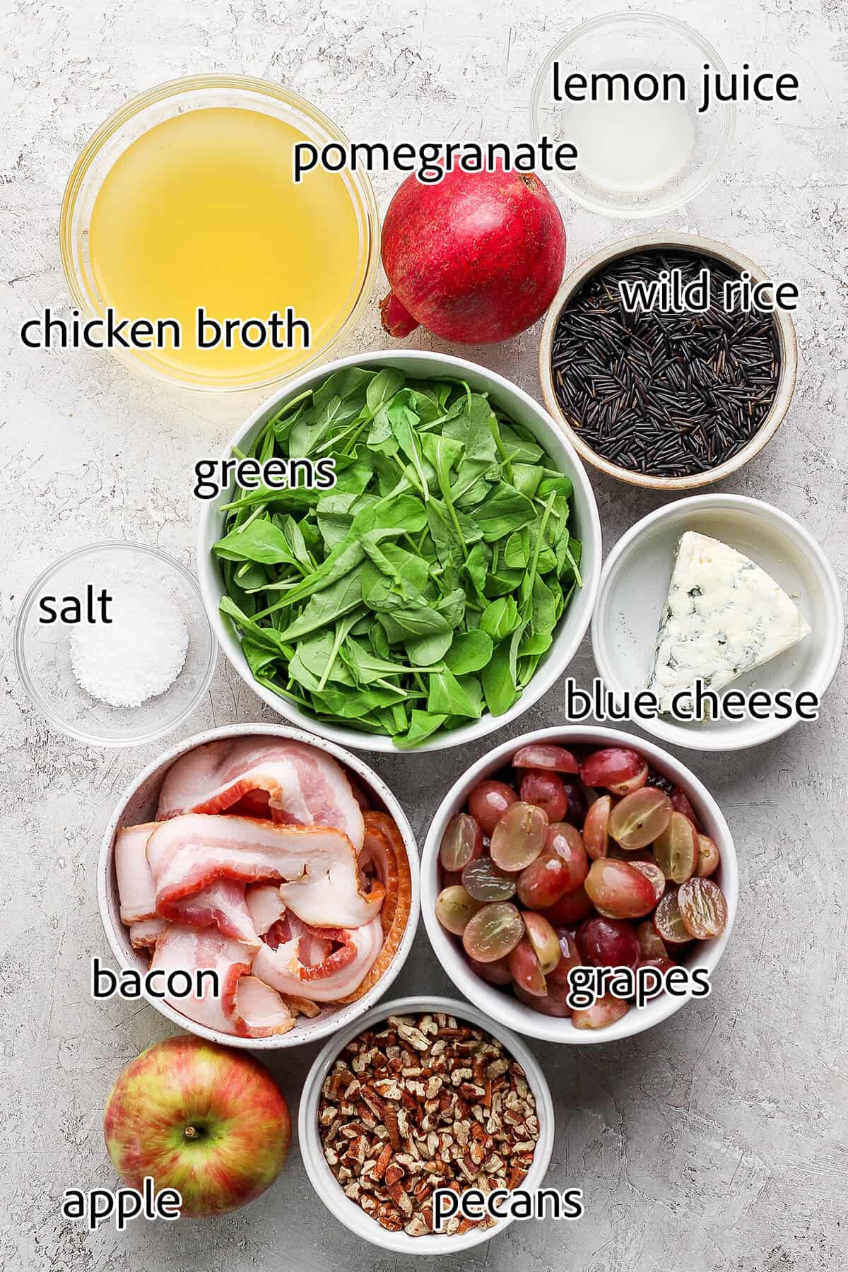 This hearty wild rice salad with pomegranate seeds, blue cheese, pecans, and maple-Dijon dressing is perfect for the holiday season. Labeled ingredients for making holiday wild rice salad.