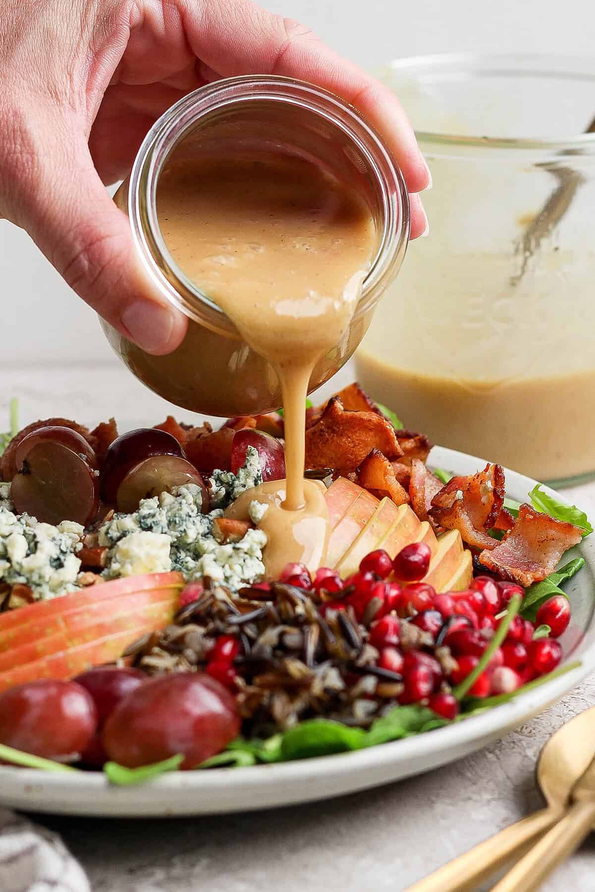 This hearty wild rice salad with pomegranate seeds, blue cheese, pecans, and maple-Dijon dressing is perfect for the holiday season. Pouring maple-Dijon dressing over the salad.