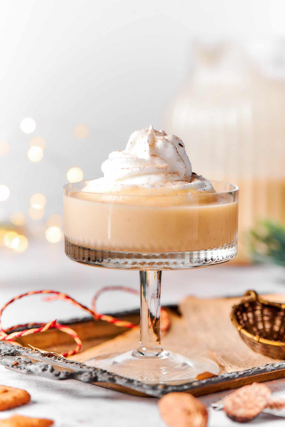 This spiced homemade eggnog recipe with brandy, smokey rum, and fluffy whipped cream is the perfect cocktail for holiday gatherings. Close-up shot of rich spiced homemade eggnog with whipped cream on top.