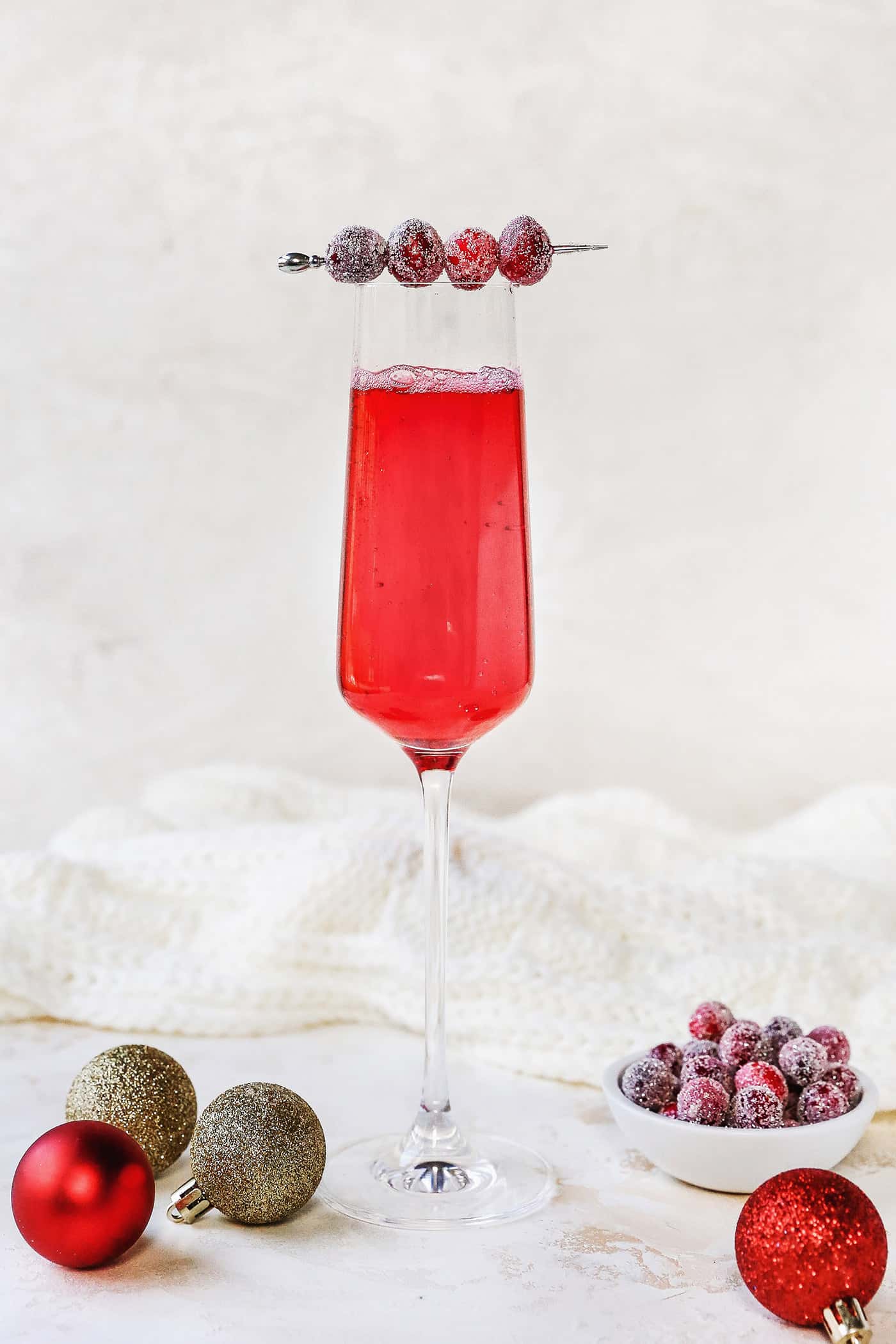 Sugared cranberries are the perfect sparkling finish for all your holiday desserts! All it takes is fresh cranberries, sugar, and water. A champagne flute filled with a cranberry cocktail, garnished with a swizzle stick of sugared cranberries.