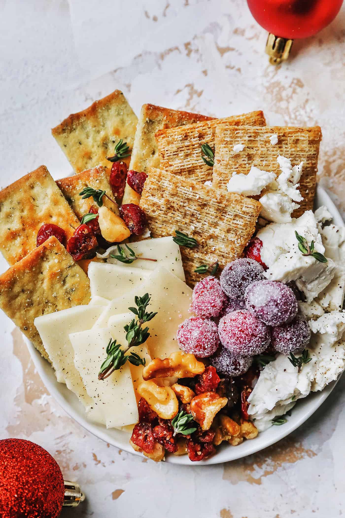 Sugared cranberries are the perfect sparkling finish for all your holiday desserts! All it takes is fresh cranberries, sugar, and water. Overhead view of a cheese plate with crackers, and nuts, and sugared cranberries for garnish.