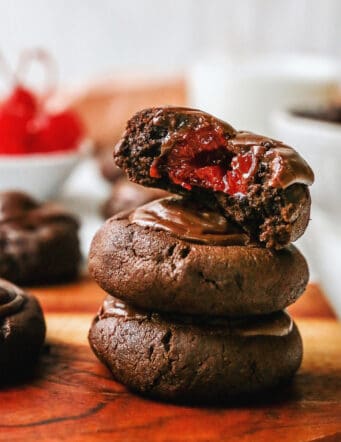 a stack of chocolate cherry cookies, one has a bite to show the cherry inside